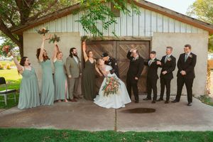 Bridal party lined up against white building wall wearing elegant blue and black formal attire.