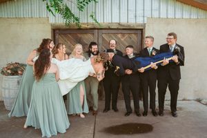 Wedding party shows off fun poses with bridesmaids in sage dresses lifting bride while groomsmen look on.