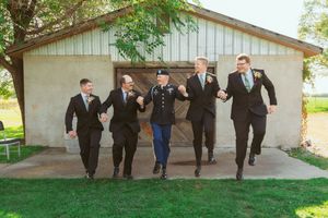 Wedding group poses playfully in a line outside venue in formal black suits and blue dresses.
