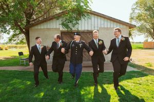 Groomsmen and bridesmaids in formal wear leap together for fun photo series outside country venue.
