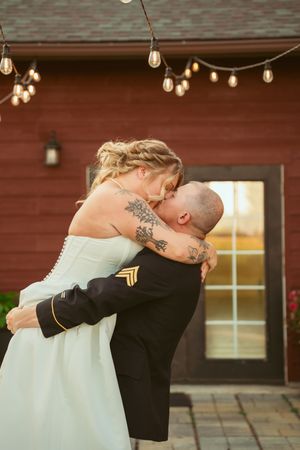 A romantic wedding moment captured under string lights outside a rustic red barn.