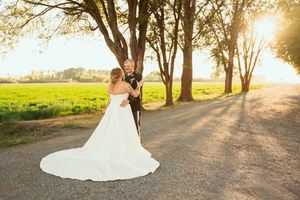 A romantic sunset wedding photo on a tree-lined country road with a flowing white wedding gown.