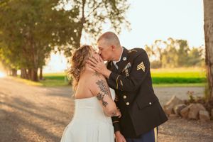 A romantic military wedding couple shares a tender moment at sunset on a tree-lined path.