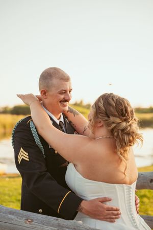 Emotional wedding moment captured between couple embracing at sunset in military dress uniform and white gown.