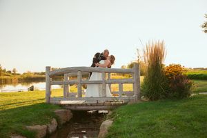 A wedding couple shares an intimate moment on a white wooden bridge at sunset near a pond.