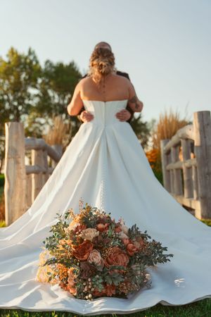 White wedding dress train with peach and green floral arrangement displayed on rustic wooden dock.