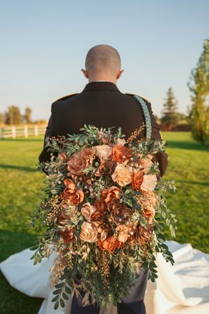 Peach and coral floral arrangement adorns black formal attire against natural outdoor setting.