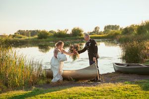 Newlyweds share a romantic moment by canoes at the water's edge during golden hour.