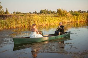 Panoramic series of wedding couple paddling in green canoes across a sunlit lake with golden reeds.