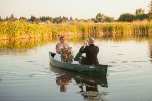 Wedding couple sits in a canoe on a serene lake surrounded by golden cattails.