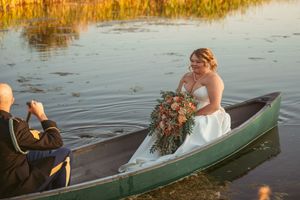 Newlyweds paddle together in green canoes across tranquil water at sunset in wedding attire.