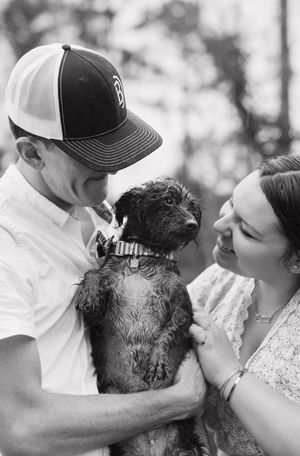 A couple shares intimate moments with their small black dog in black and white portraits.