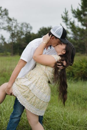 A couple embraces romantically in a grassy field on a cloudy day.