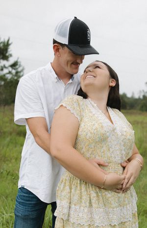 Romantic couple embracing in a grassy field wearing white and yellow floral dress.