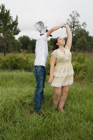 Couple sharing a joyful moment while dancing in tall grass with trees in distance.