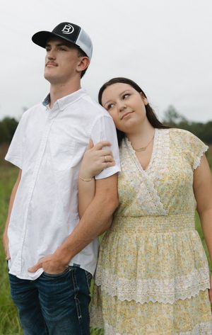 Couple in casual attire posing together in field wearing white shirt and yellow dress.