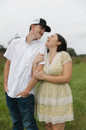 Couple sharing laughter and embrace in grassy field on cloudy day.