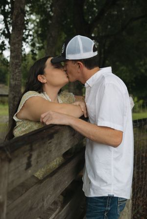 A romantic couple sharing an intimate kiss while leaning against a tree trunk in a natural outdoor setting.