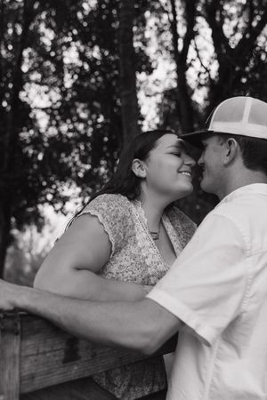 Black and white photo of romantic couple embracing outdoors with trees in background.