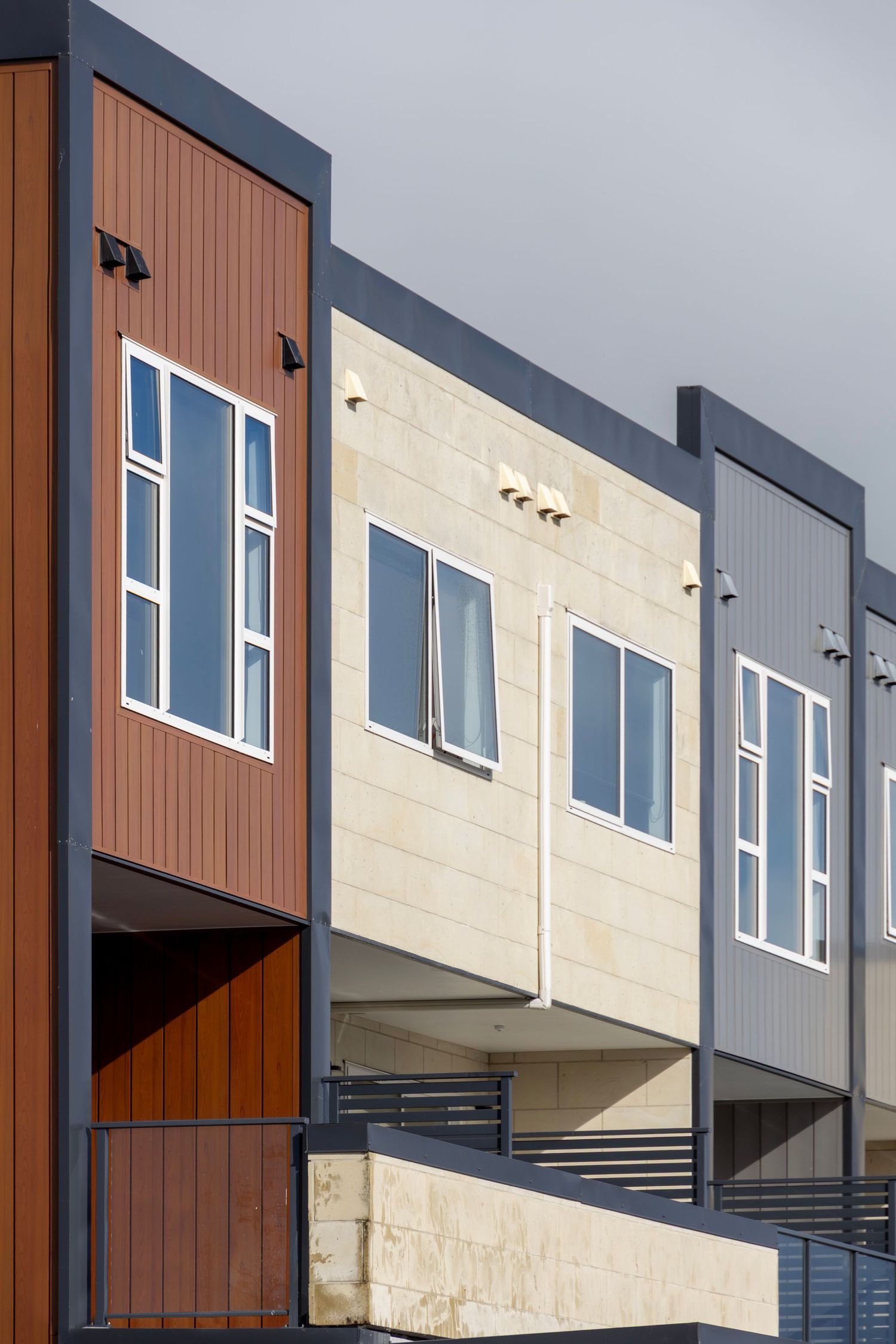 Modern apartments with panelled cladding in timber, stone, and black framing against a grey sky.