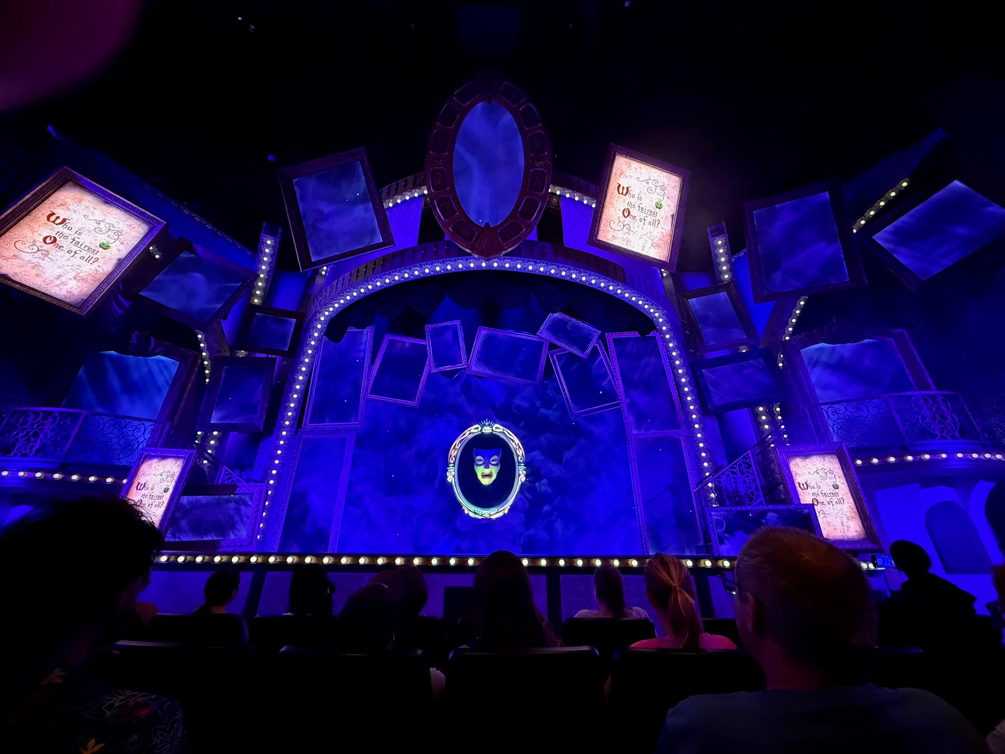 Theater stage with blue lighting and illuminated digital screens in a dark auditorium.