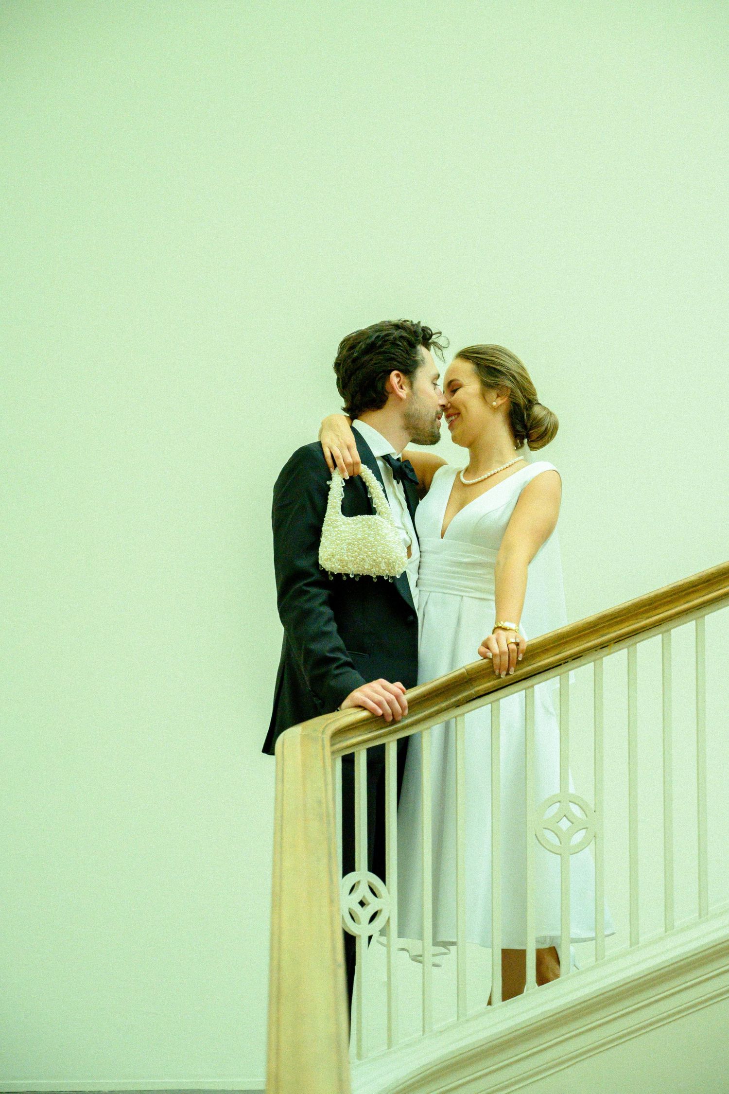 A romantic couple in formal attire shares an intimate kiss by a white staircase railing in an artistic sequence.