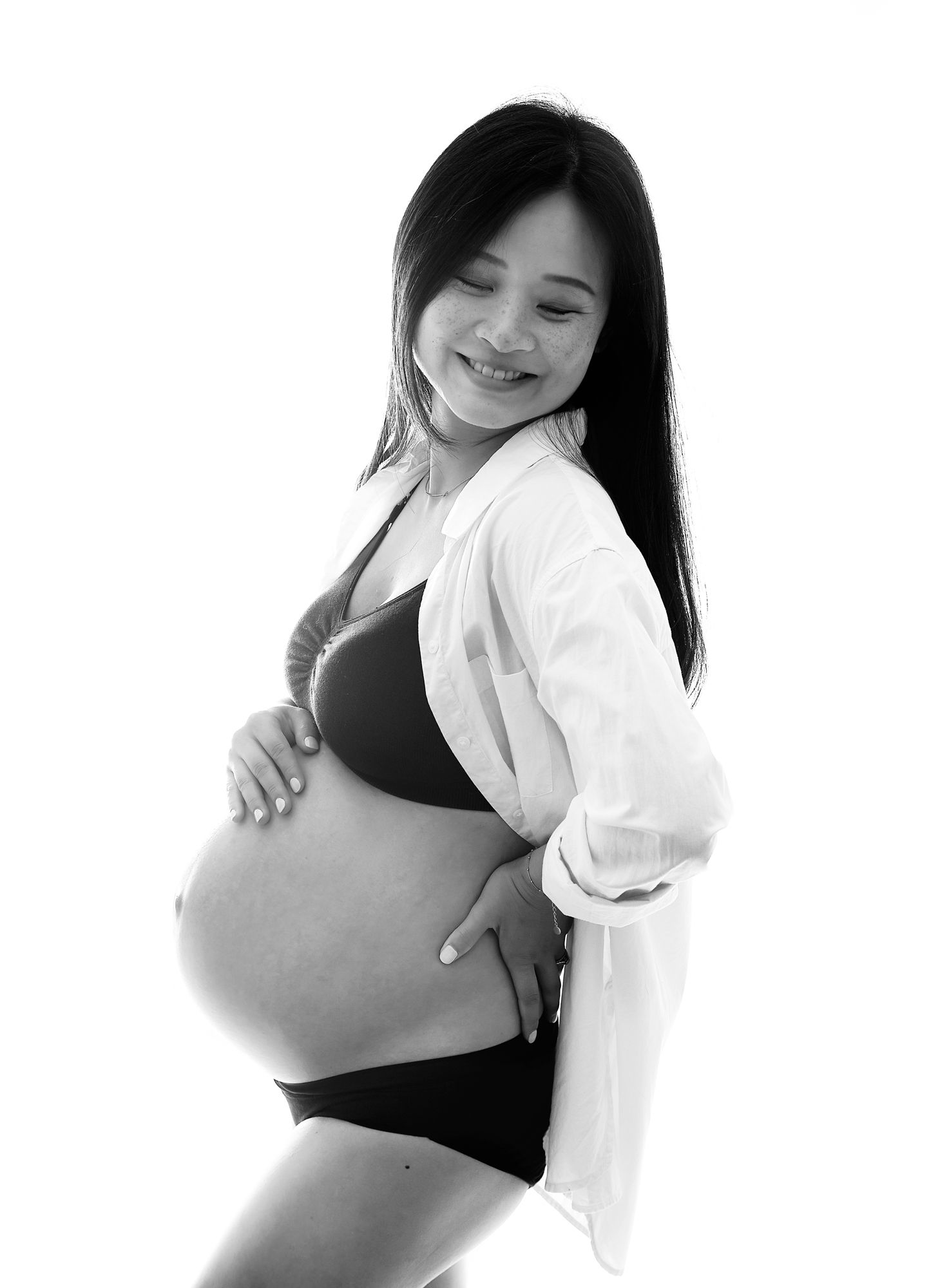 Black and white maternity photo showing an intimate moment between a couple gazing at a pregnant belly. During a London maternity photoshoot