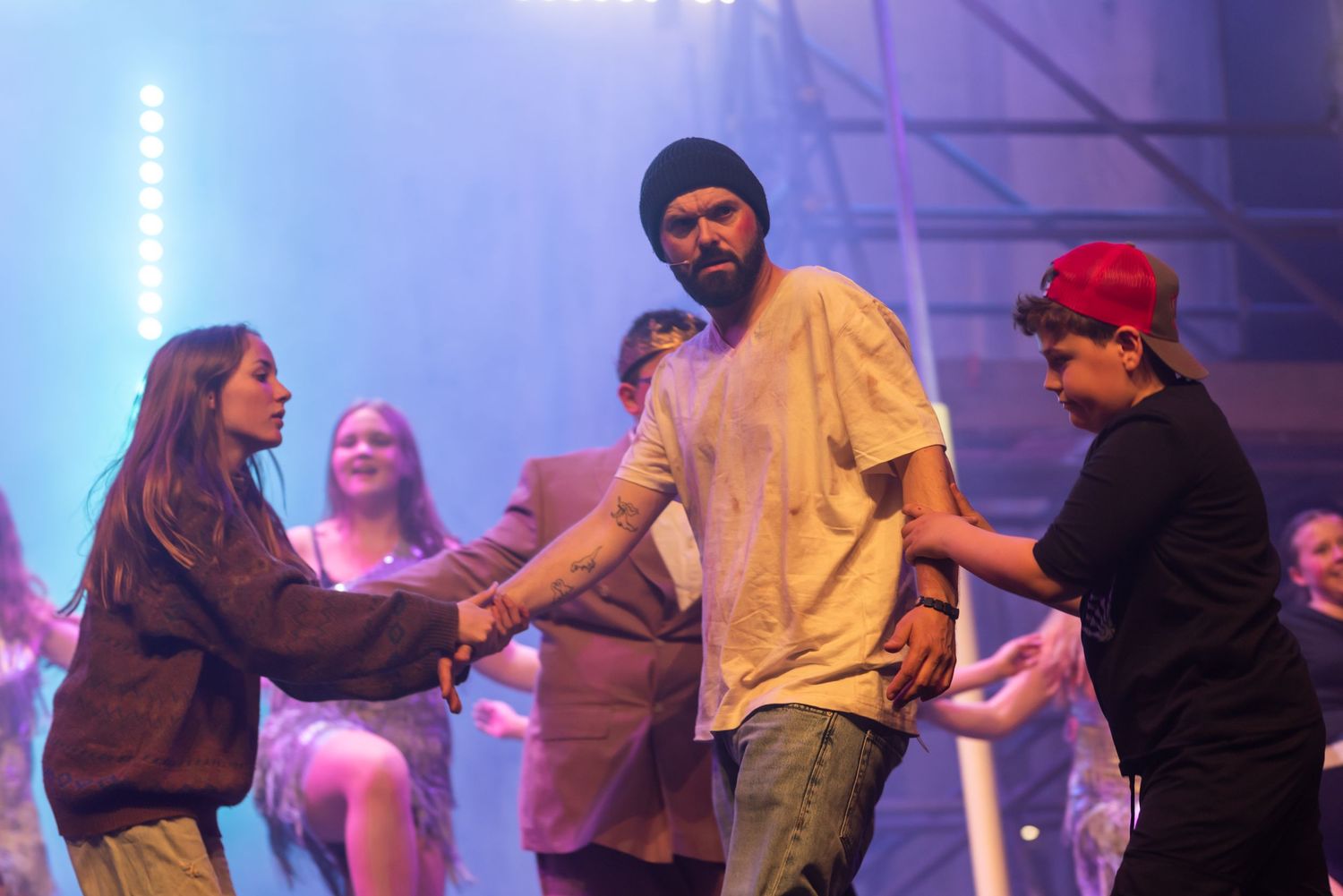 People performing on stage with blue lighting and theatrical effects.
