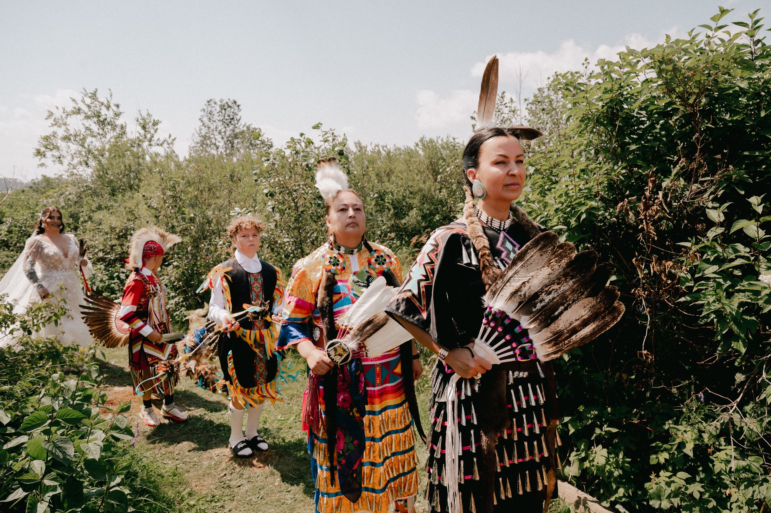 Traditional Scottish performers in kilts and ceremonial dress walking in procession through a garden pathway.