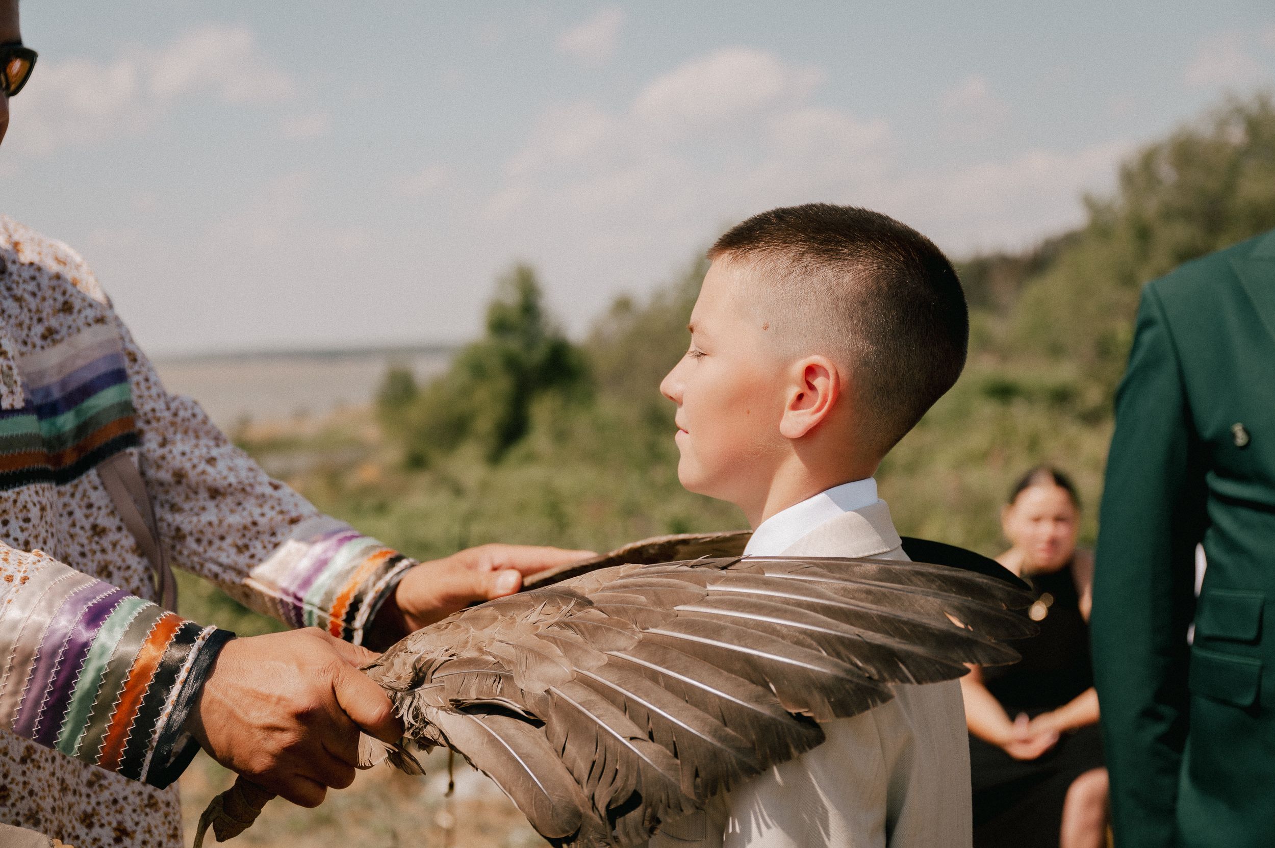Someone's arm stretches to touch a large brown bird wing in an outdoor setting during daytime.
