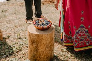 A decorated terracotta bowl sits atop a wooden stump next to colorful traditional clothing outdoors.