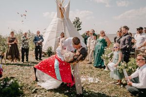A dipping kiss shared between newlyweds at an outdoor wedding ceremony with a teepee and onlooking guests.