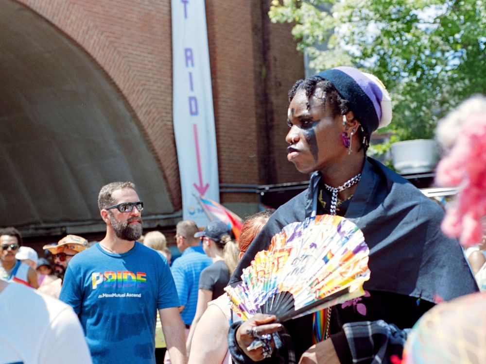 Attendee at an outdoor festival waves a decorative fan while wearing a navy blue outfit and cap among the crowd.