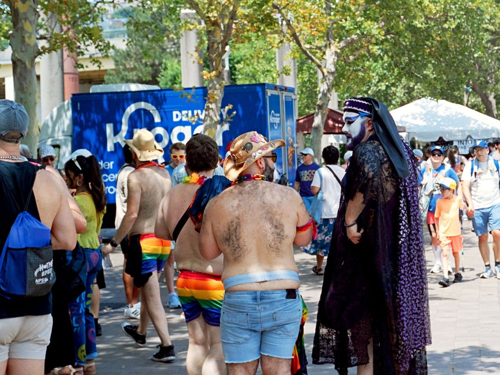 Festival crowd in summer attire gathered near a blue portable restroom station.