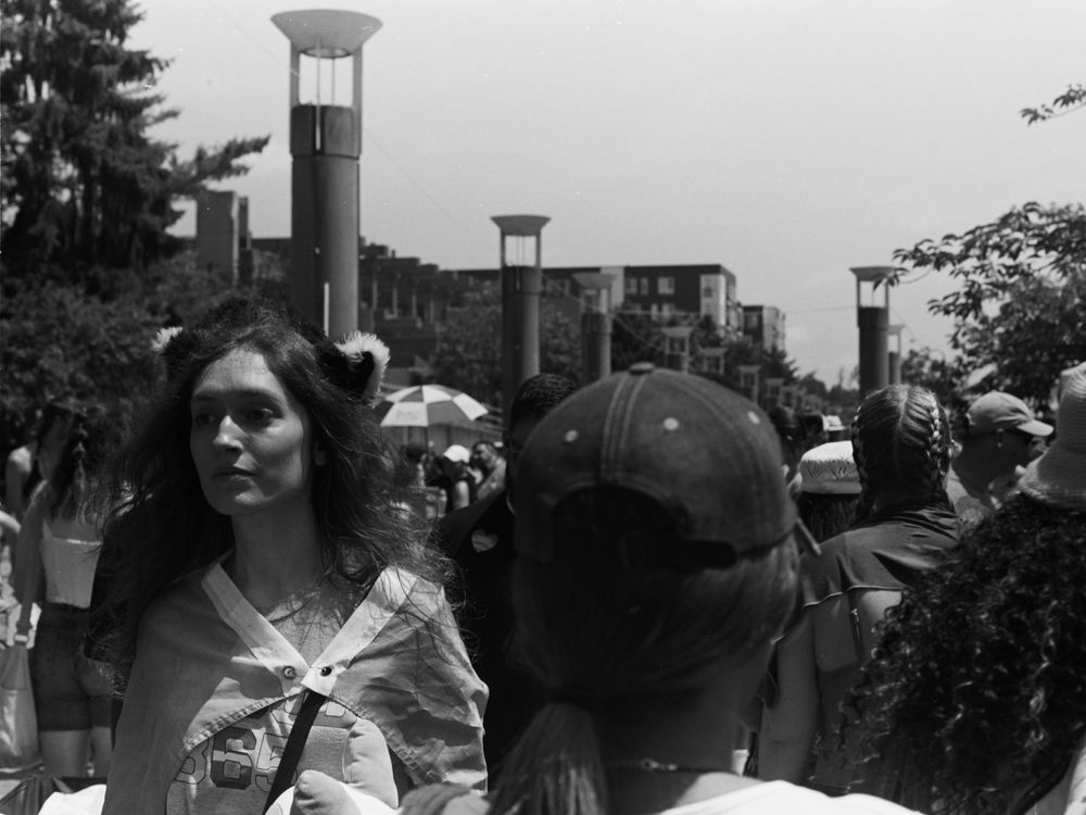 People walking on a campus pathway with tall lamp posts and buildings visible in the background in black and white.