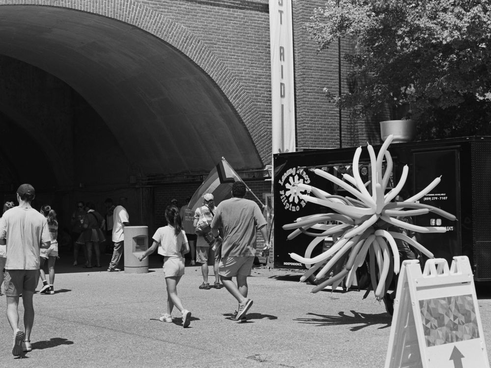 People walk past a large sculptural art installation near an archway entrance.