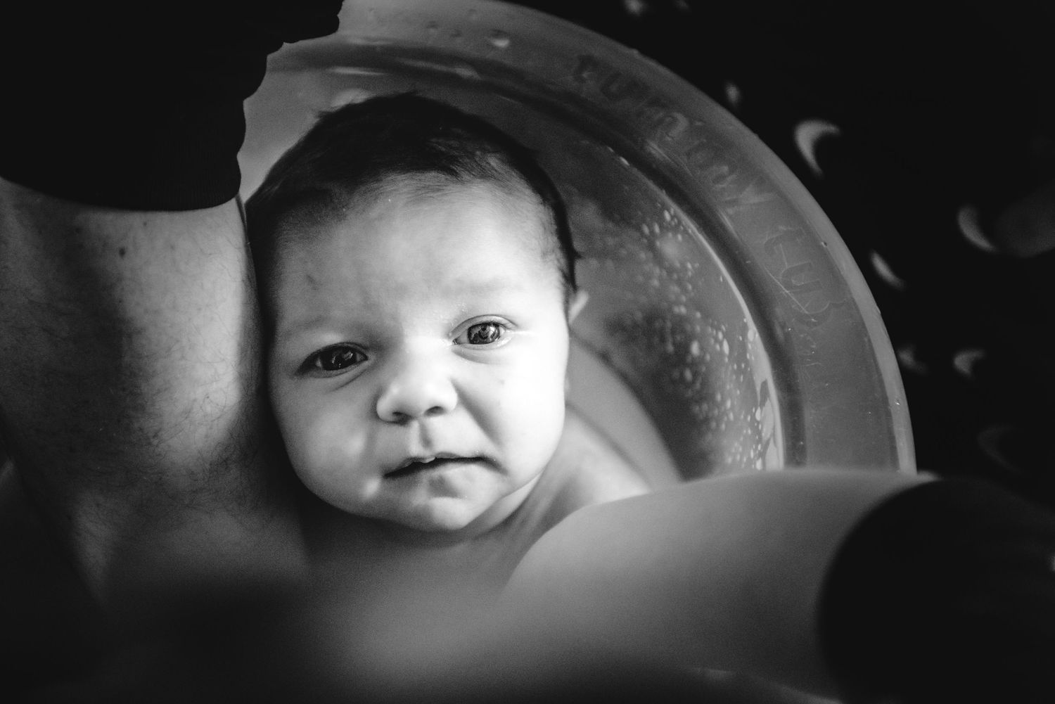 Black and white portrait of a baby looking up as they're being bathed.