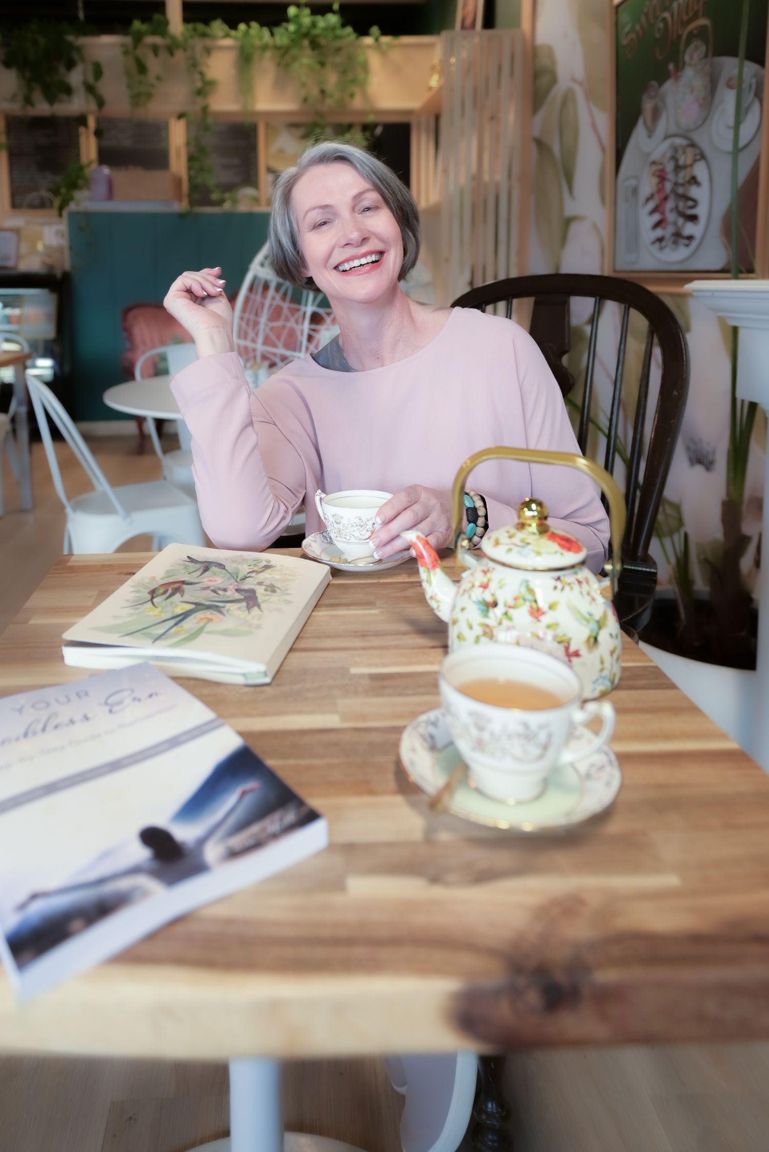 Cozy cafe scene with teapot and treats on wooden table in natural lighting.
