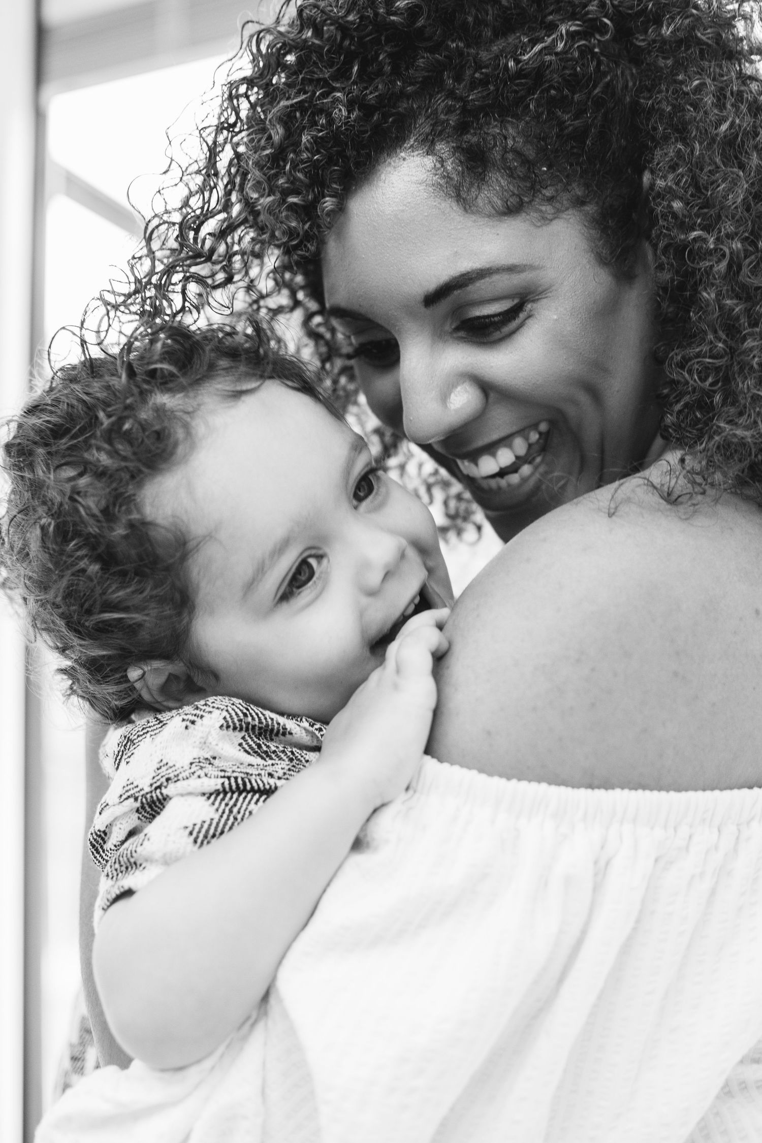 Black and white portrait of a parent and child with curly hair sharing a tender moment together.