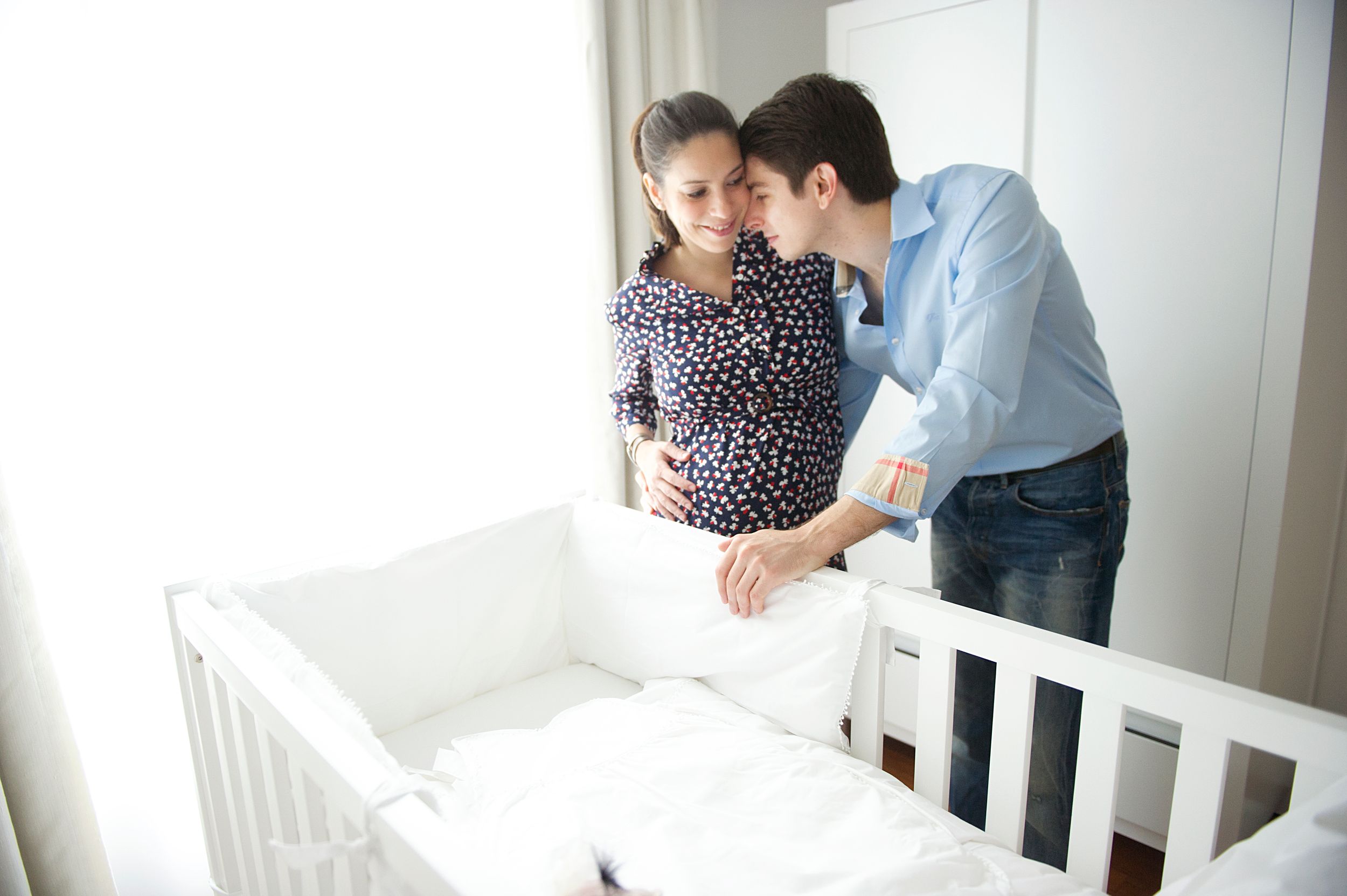 Expecting parents set up a white wooden crib while preparing a nursery in a bright room. Captured by GTA maternity photographer Phoebe Lee.