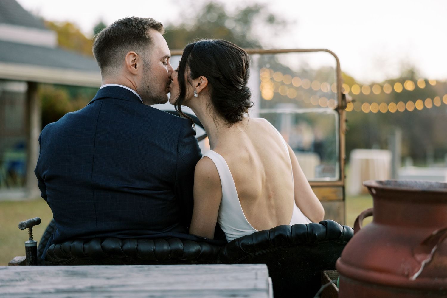 A romantic couple sitting close together on a bench with string lights glowing in the background.