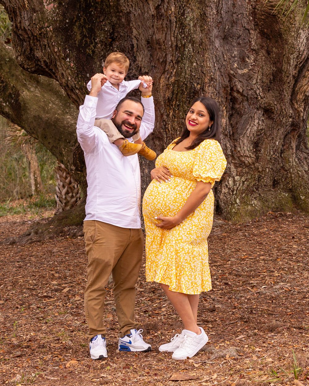 Playful family photo with child held up high against tree backdrop.