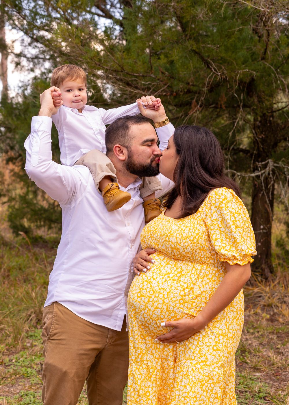 Intimate family portrait with toddler sitting on shoulders while parents share a moment.