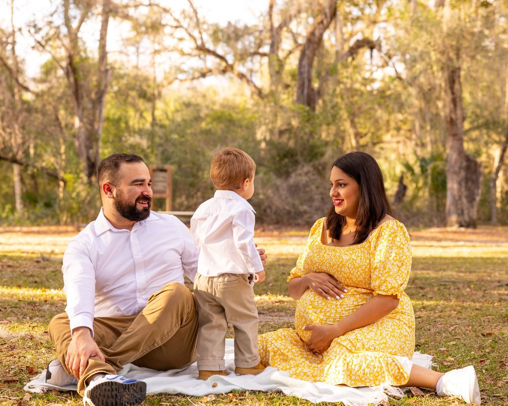 Family enjoys picnic on blanket in park with palm trees in background.