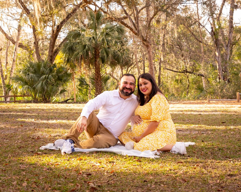 Couple sits together on blanket in sunny park setting.