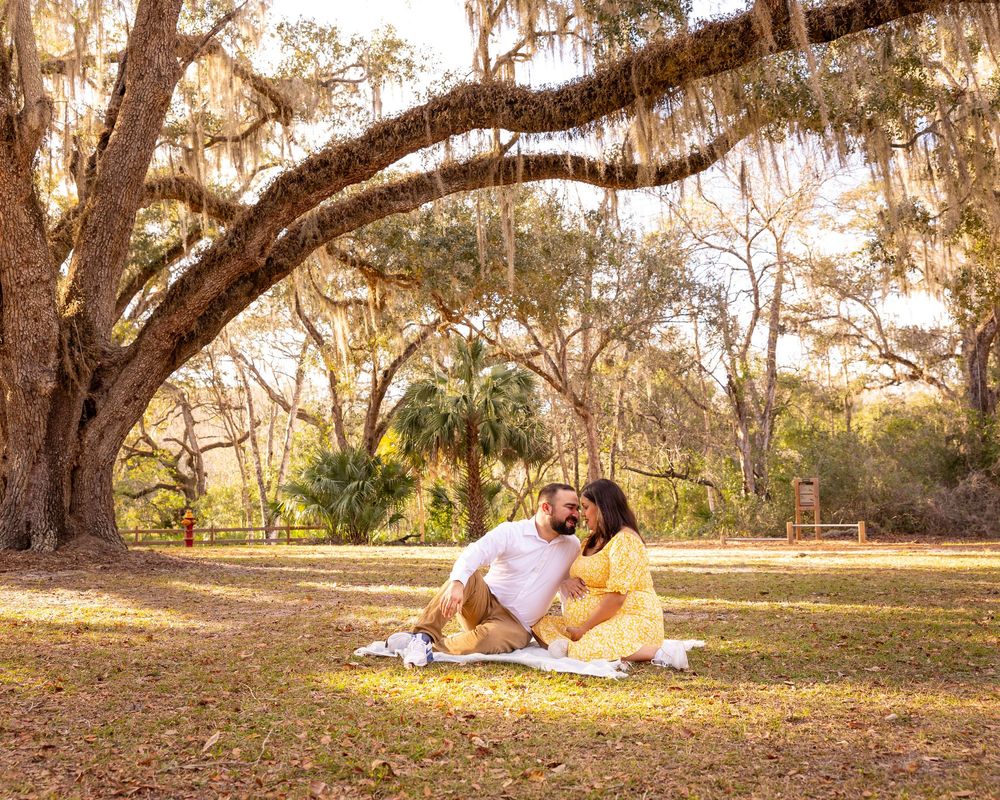 Couple relaxes on picnic blanket under sprawling oak tree in park.