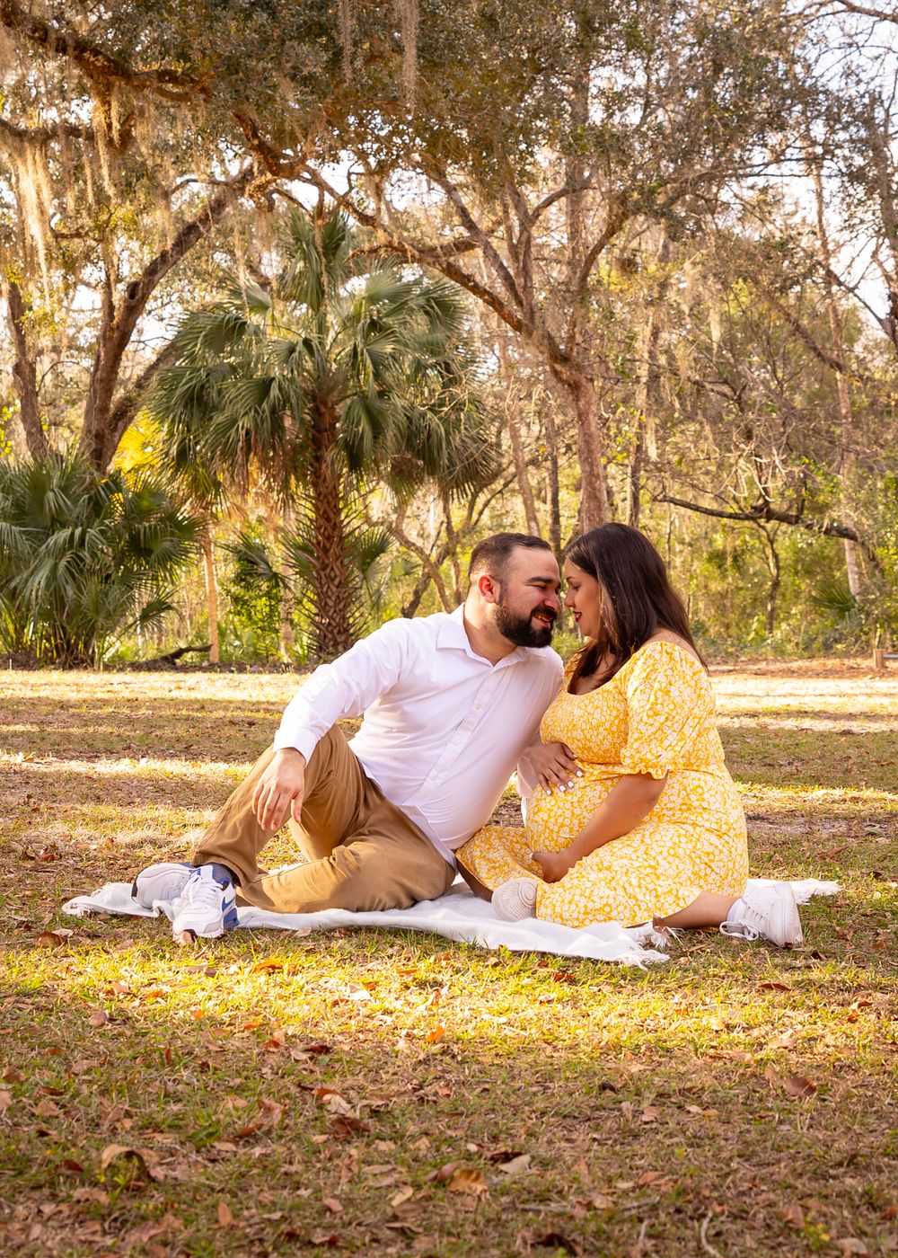 Couple shares intimate moment while sitting on blanket in sunlit park.