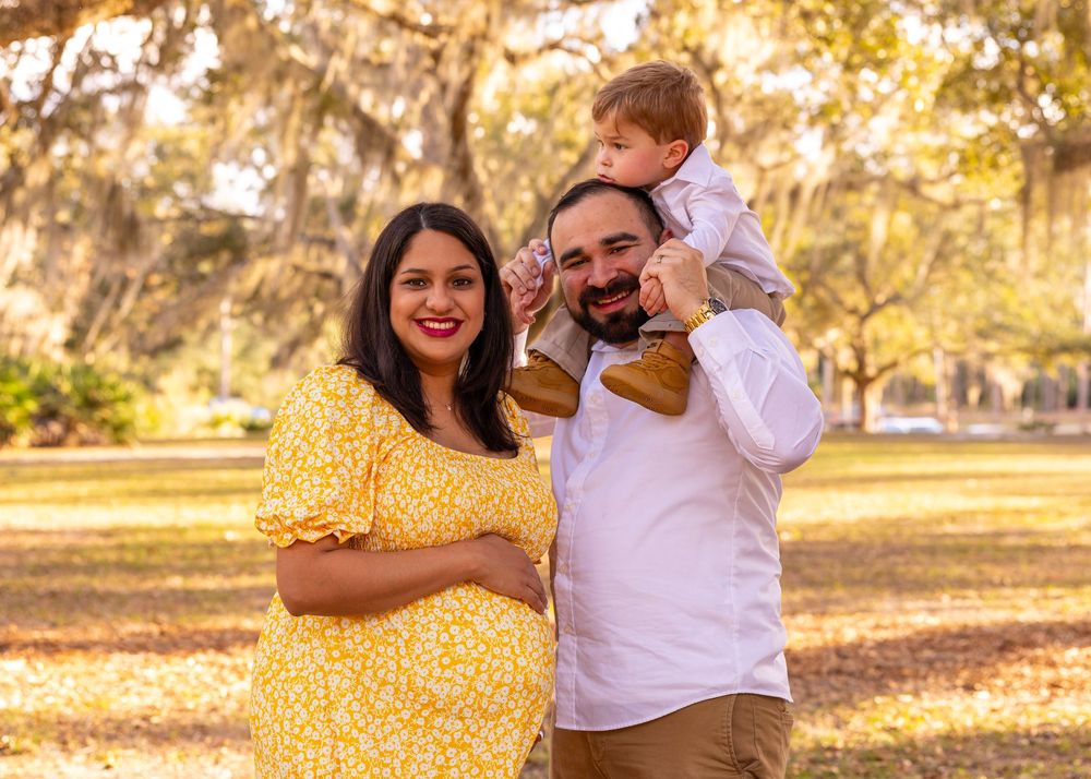 Family shares joyful moment outdoors with autumn trees in background.