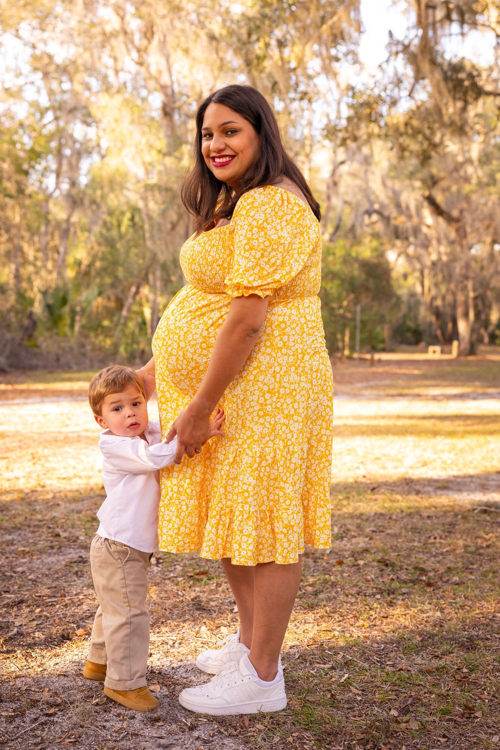 A young child hugs a person wearing a cheerful yellow floral dress in a sunny outdoor setting.