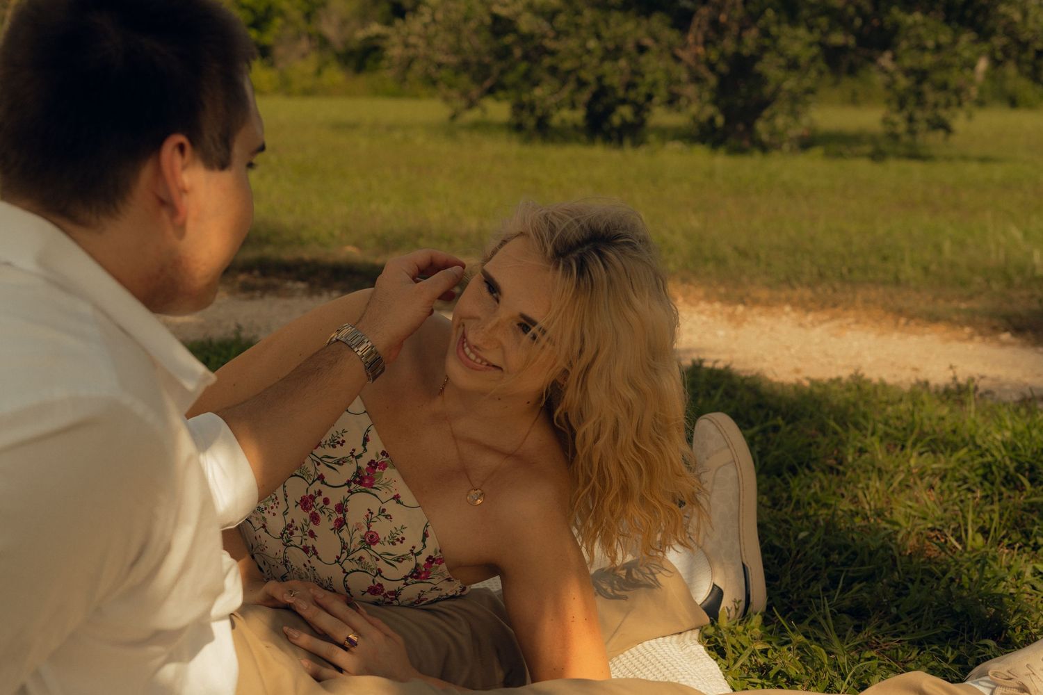 m/f couple standing close together - cuddled into him - at a lake with greenery surrounding.